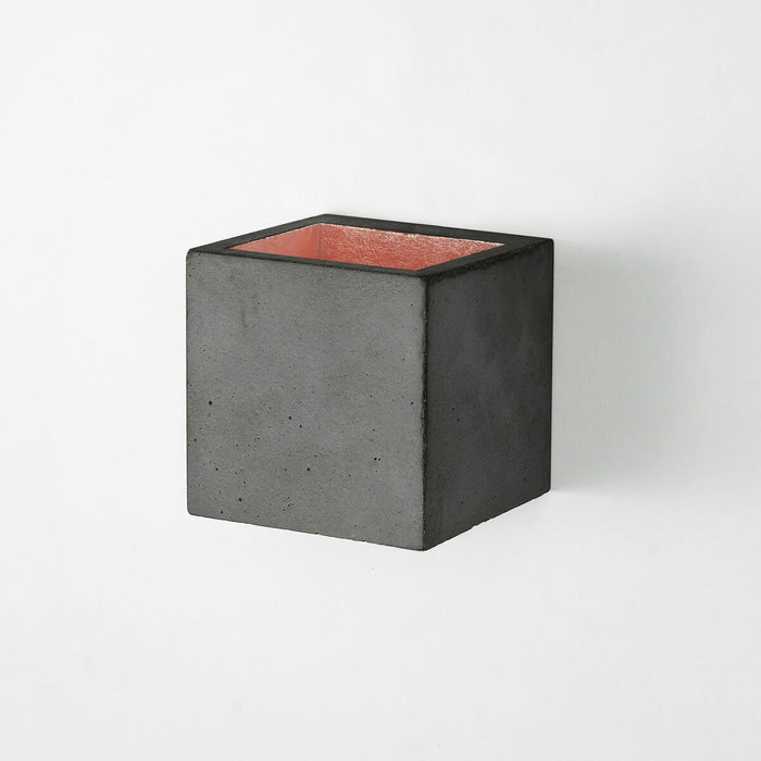 Wall light in 10cm cubic shape made from dark grey concrete with a copper coloured inside plating