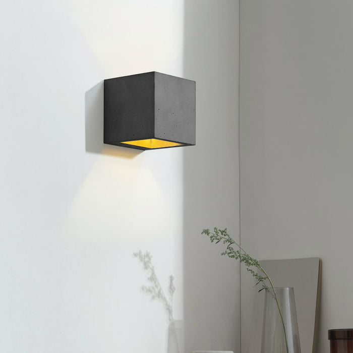 Wall light in 10cm cubic shape made from dark grey concrete with a gold coloured inside plating